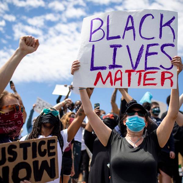 Demonstrierende sind auf der Straße nach dem Tod von George Floyd unterwegs. Eine Frau hält ein „Black Lives Matter“-Schild in die Luft.