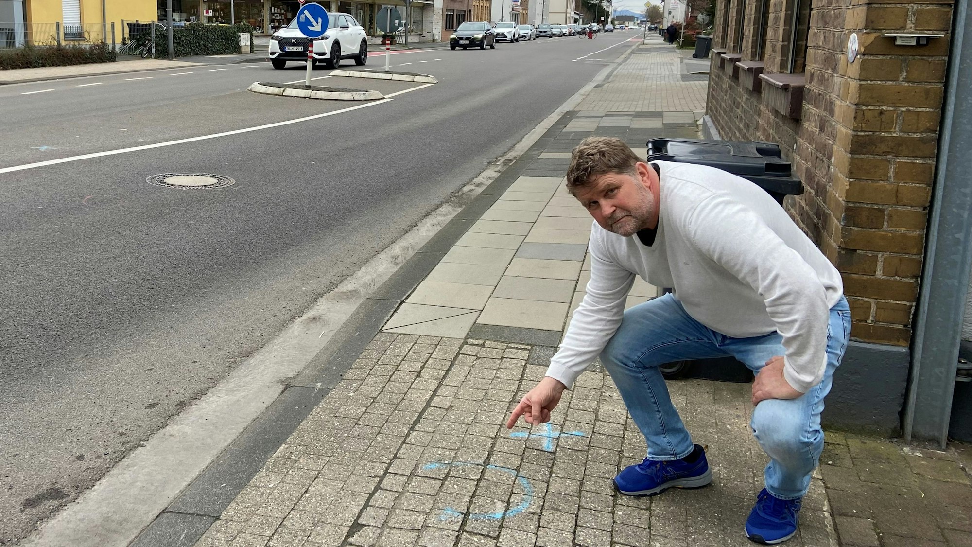 Mann, der auf einem Bürgersteig in die Hocke geht und auf diesen zeigt.