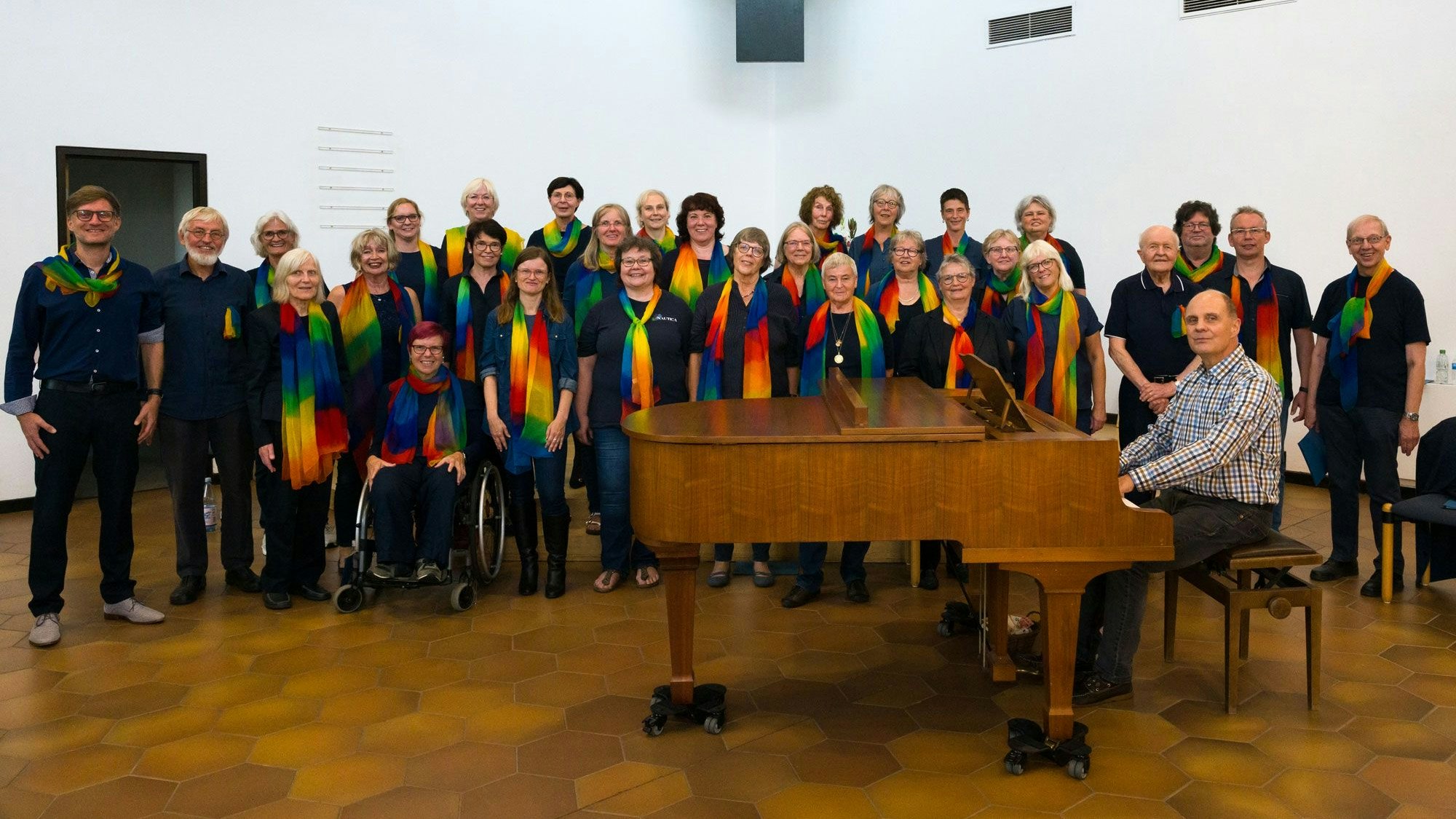 Der Gospelchor Altenberg steht in zwei Reihen hinter einem Klavier, an dem der verstorbene Chorleiter Andreas Ohle sitzt.