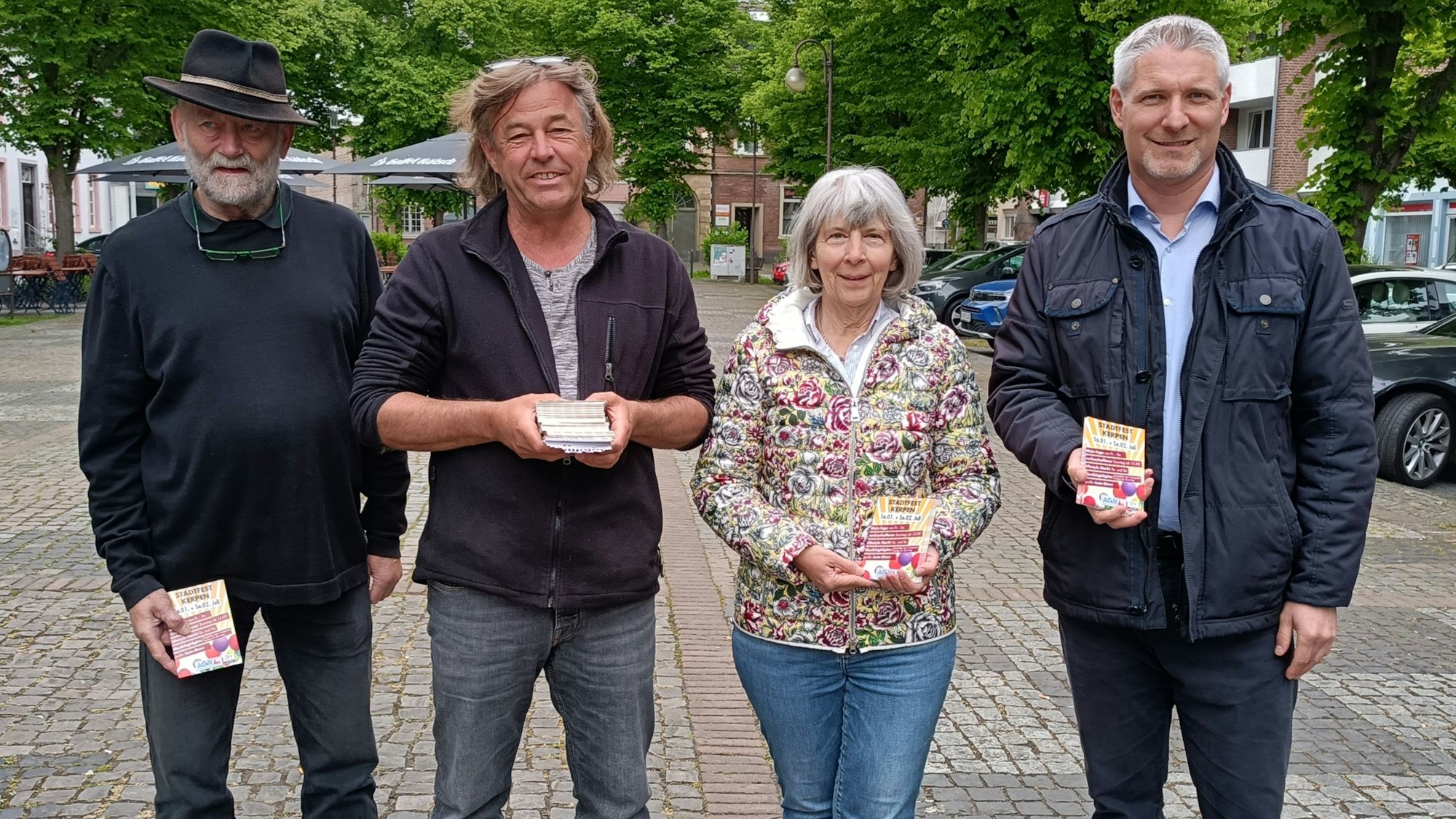 Es sind die vier genannten Personen zu sehen, die mit den Flyern in den Händen nebeneinander stehen.