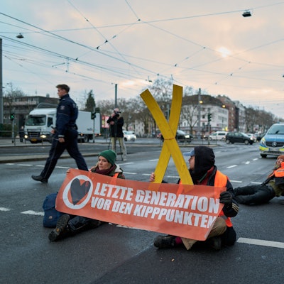 Aktivisten der „Letzten Generation“ kleben sich auf der Fahrbahn fest – Polizisten tragen Aktivisten von der Fahrbahn.