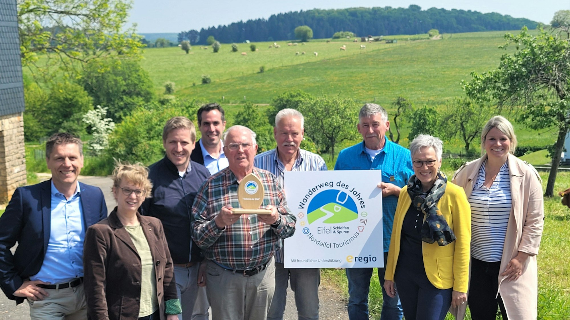 Das Bild zeigt eine Gruppe von Personen vor einer grünen Wiese. Drei Männer halten die Auszeichnungen, die ihnen verliehen wurden.