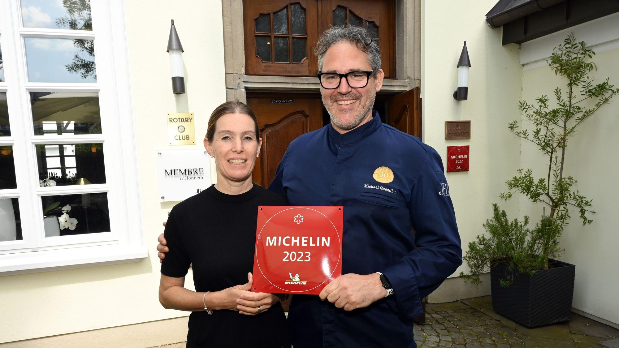 Ein Ehepaar steht vor seinem Restaurant, mit der Auszeichnung „Michelin 2023“ in den Händen
