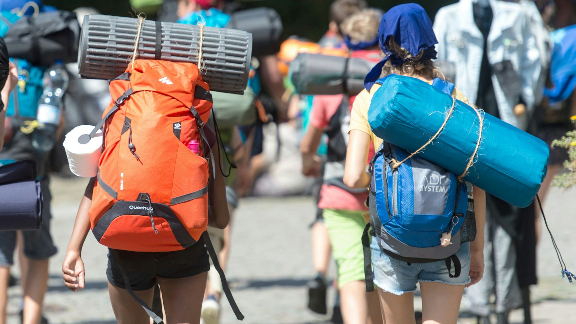 Reisende Jugendliche gehen mit ihren Rucksäcken und aufgeschnallten Schlafmatten durch die Innenstadt.