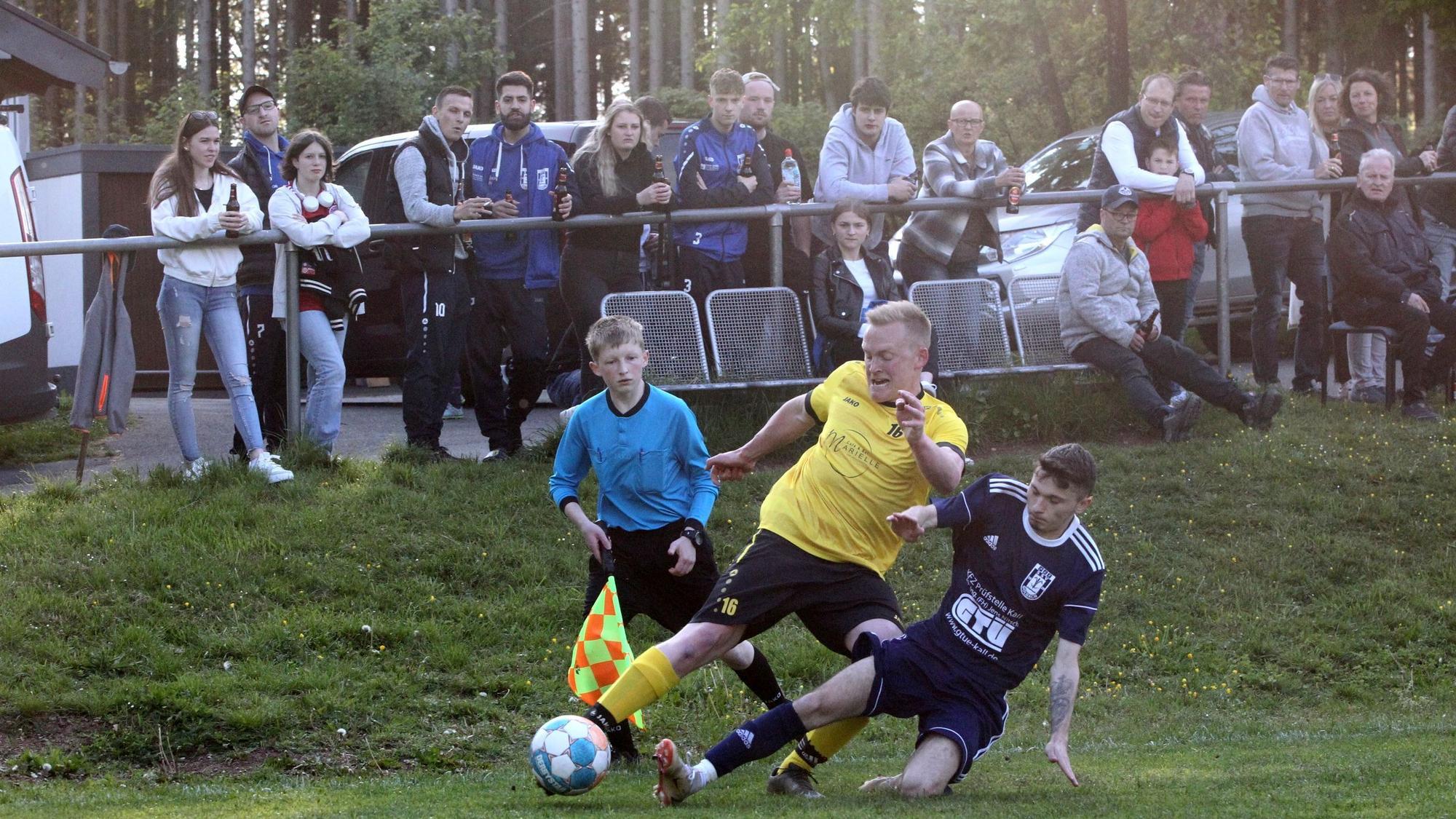 Dominik Fink und ein Golbacher Gegenspieler gehen direkt vor den Augen des Schiedsrichter-Assistenten in den Zweikampf. Im Hintergrund zahlreiche Zuschauer.
