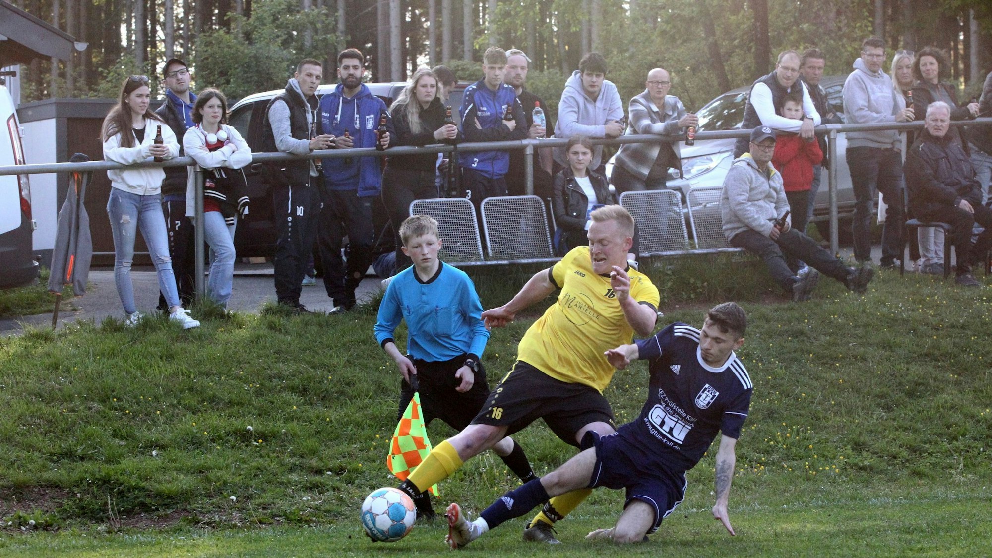 Dominik Fink und ein Golbacher Gegenspieler gehen direkt vor den Augen des Schiedsrichter-Assistenten in den Zweikampf. Im Hintergrund zahlreiche Zuschauer.
