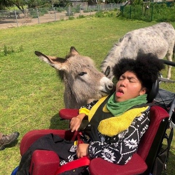 Die 15-jährige schwerst beeinträchtige Eloisa sitzt im Rollstuhl, eine Eselin stupst ihr leicht an die Wange.