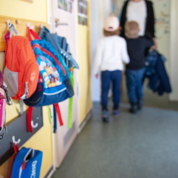 Das Foto zeigt die Garderobe in einer Kita. An den Haken hängen bunte Rucksäcke.