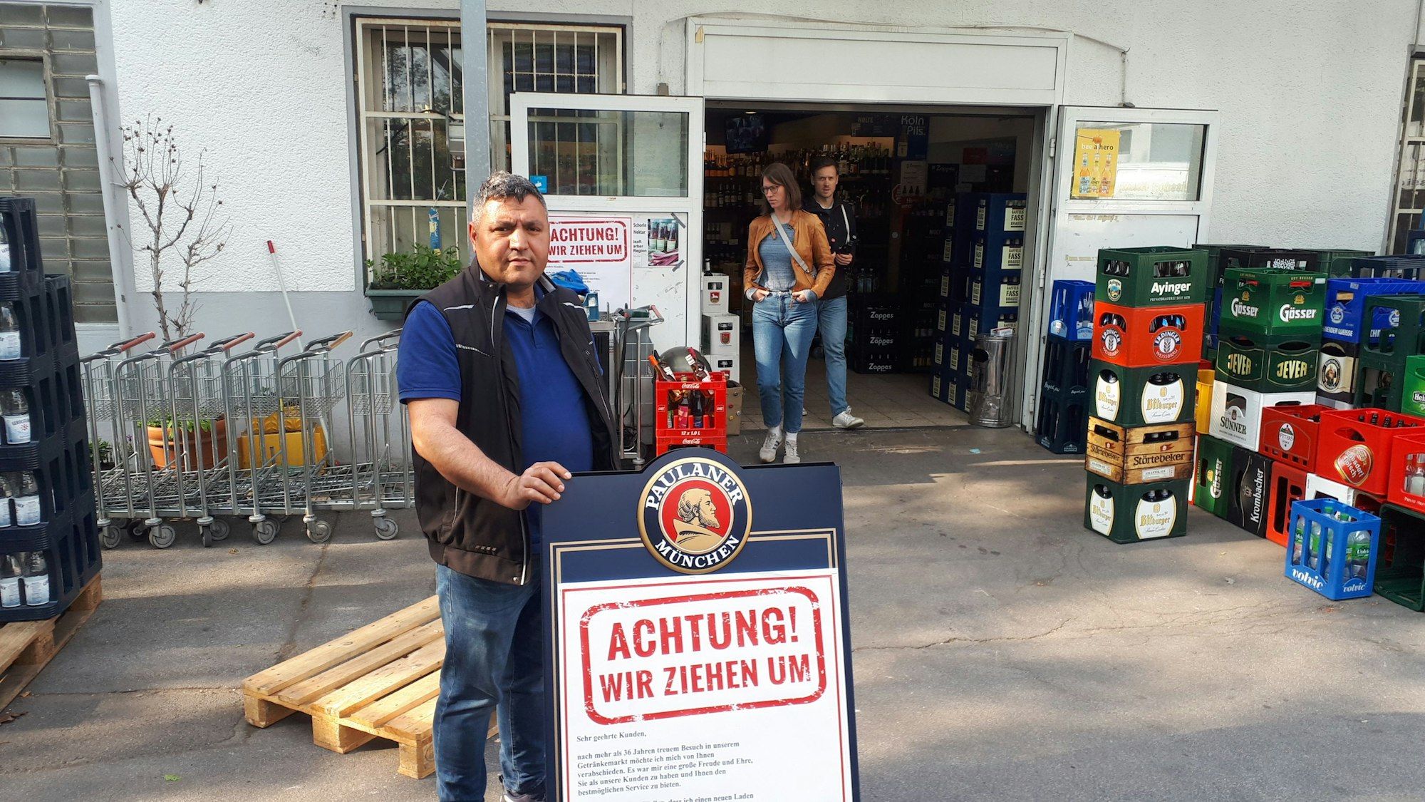 Der Chef des Getränkemarktes steht an einem Schild, auf dem steht, dass der Laden schließt.