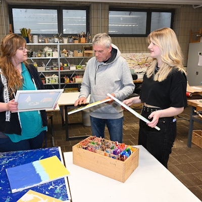 Es sind die drei genannten Personen mit Leinwänden in der Hand zu sehen.