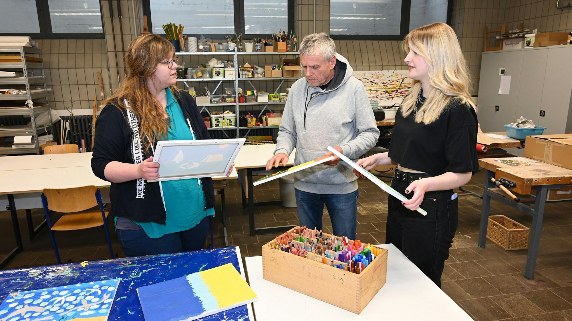 Es sind die drei genannten Personen mit Leinwänden in der Hand zu sehen.