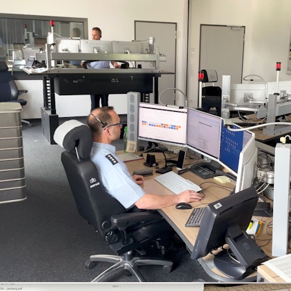 Ein Polizist in Uniform sitzt an einem Computerarbeitsplatz vor vier Bildschirmen.