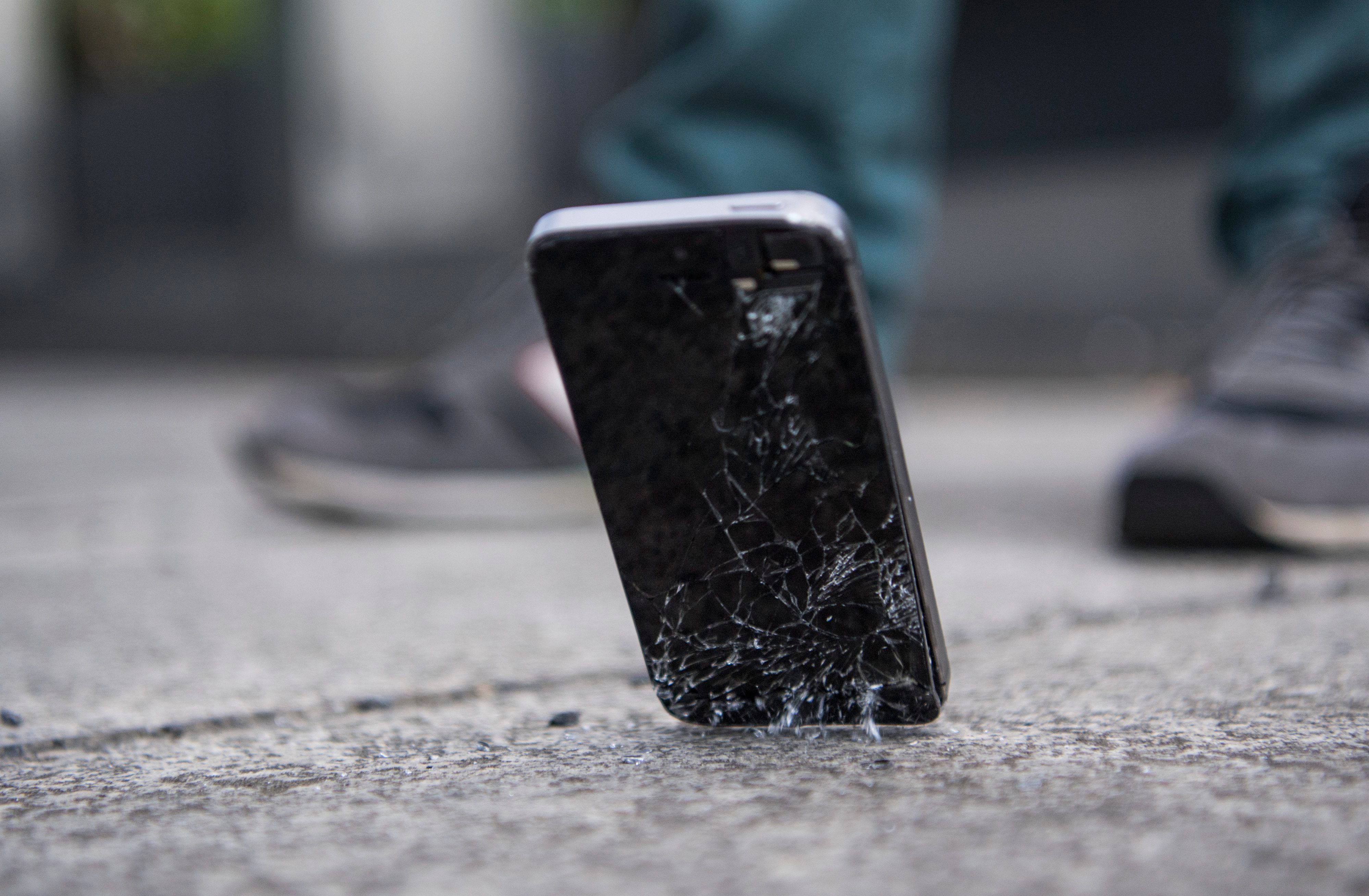 Ein Handy mit kaputtem Bildschirm fällt auf den Boden.
