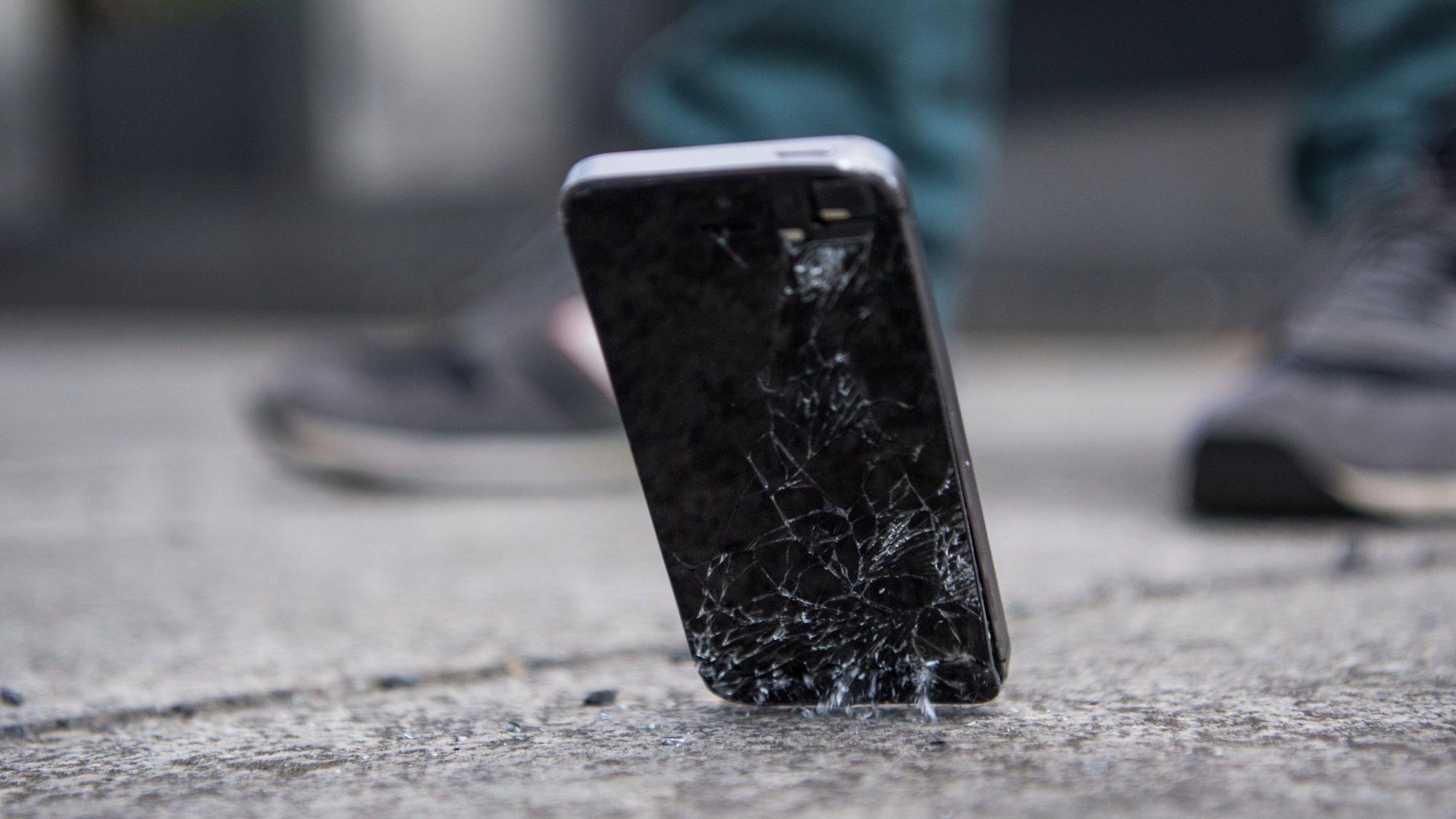 Ein Handy mit kaputtem Bildschirm fällt auf den Boden.
