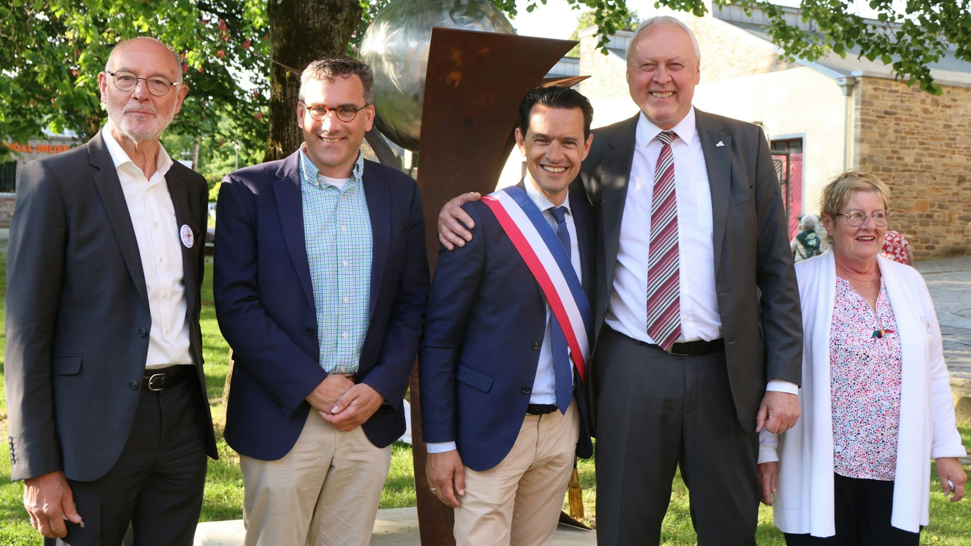 Die beiden Bürgermeister und Vertreter der Partnerschaftskomitees stehen gemeinsam vor der enthüllten Skulptur auf dem Engels-Platz.