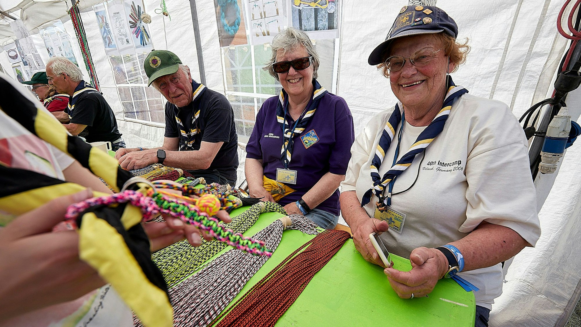 Das Bild zeigt zwei Frauen und einen Mann in Pfadfinder-Kleidung, die einen Knoten-Workshop durchführen.