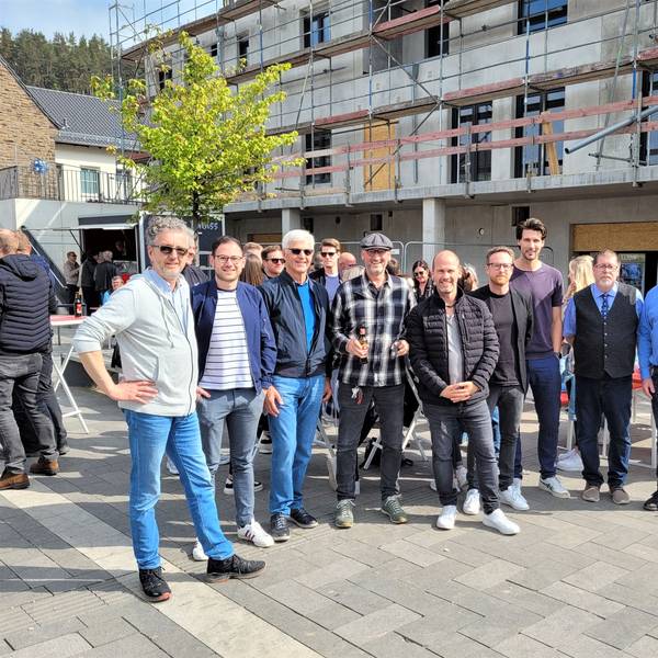Eine Gruppe Menschen steht vor einem Neubau, an dem Richtfest gefeiert wird.