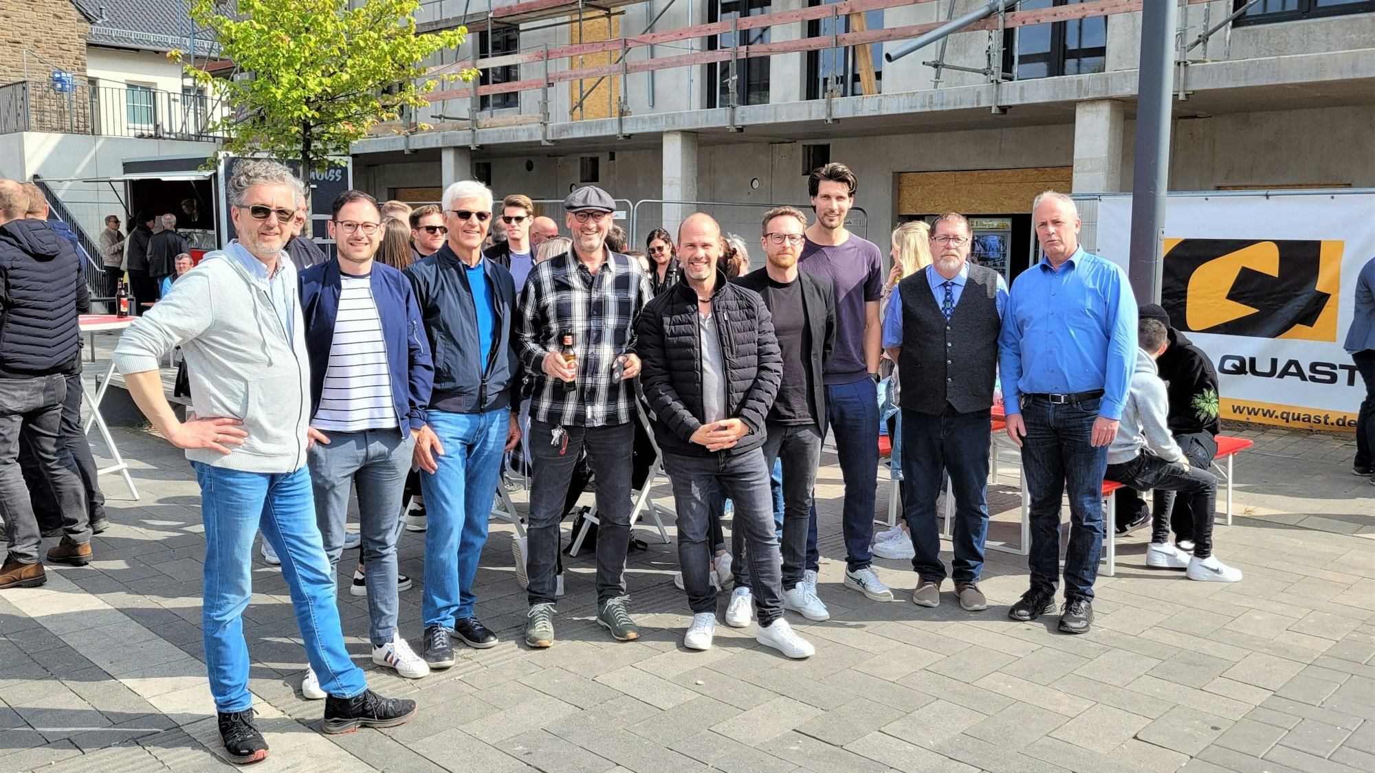 Eine Gruppe Menschen steht vor einem Neubau, an dem Richtfest gefeiert wird.