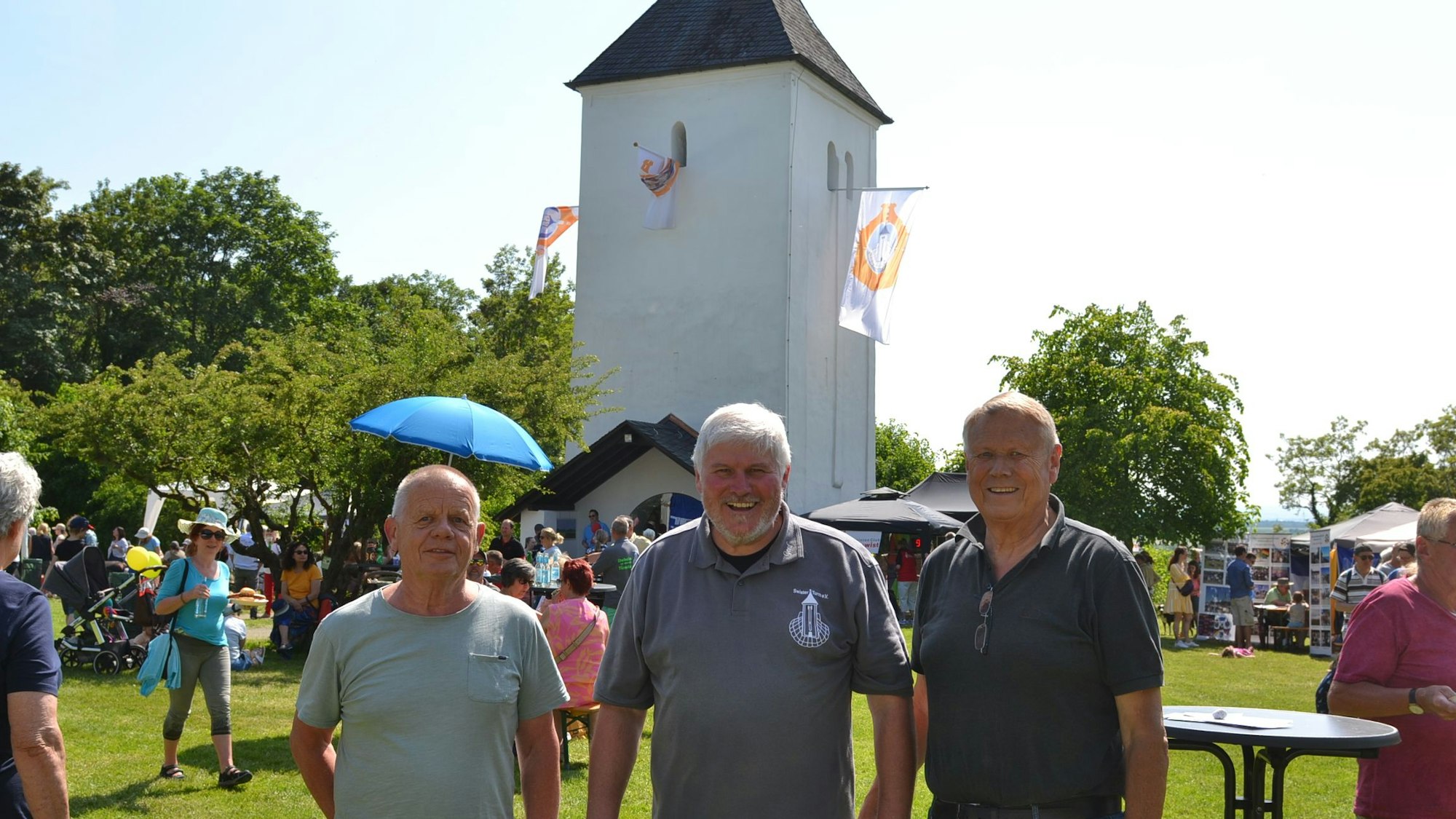 Drei Männer sind vor dem Swister Tum zu sehen, im Hintergrund ist die Festwiese.