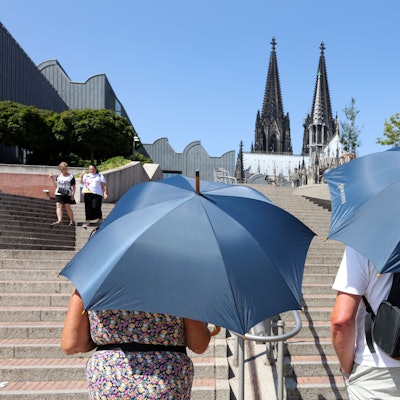 Zwei Touristen laufen mit Regenschirmen, die als Sonnenschirme genutzt werden, auf den Dom zu.