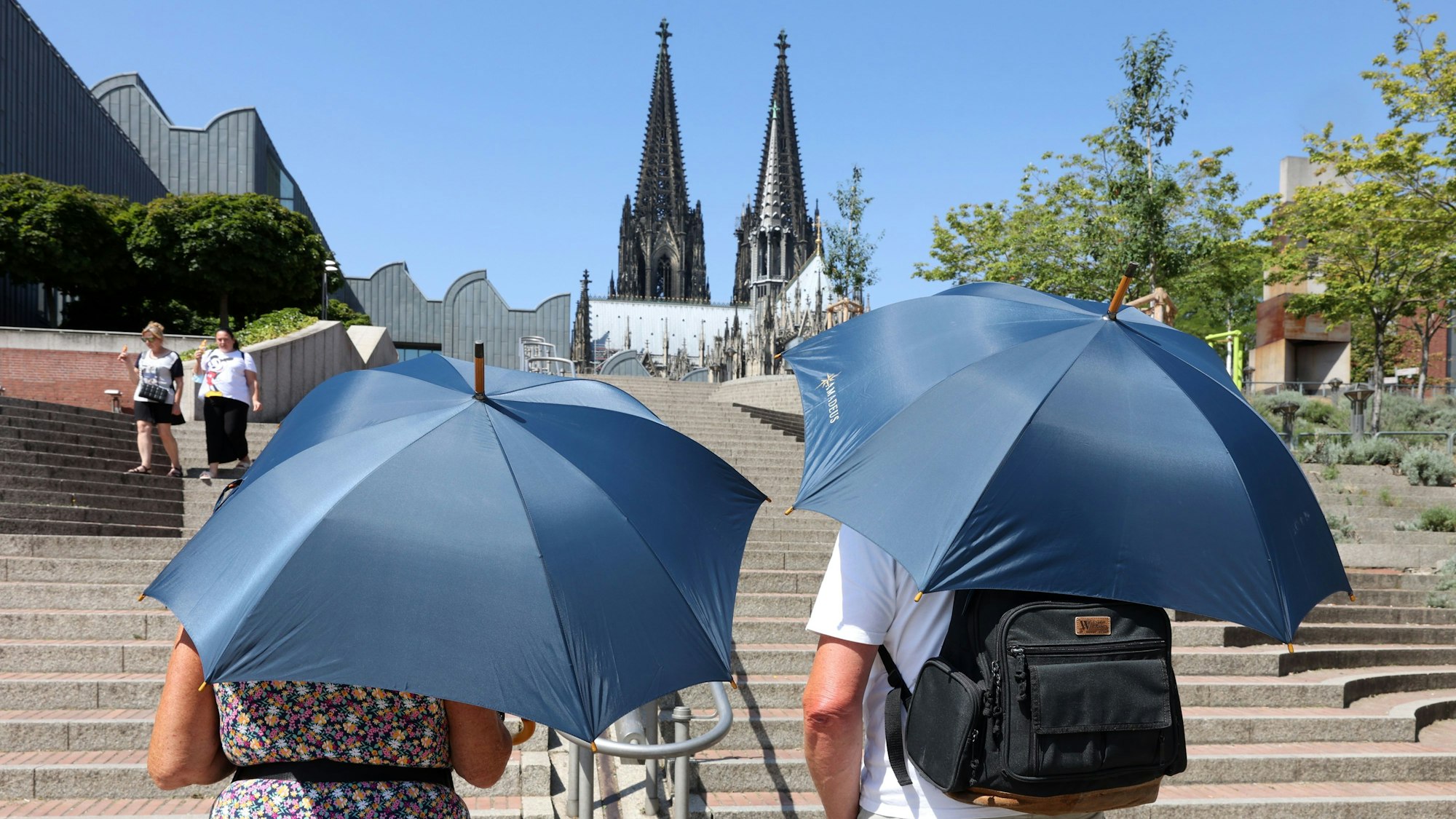 Zwei Touristen schützen sich mit Regenschirmen vor der Sonne.