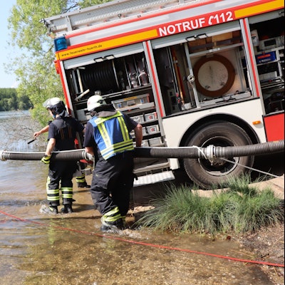 Ein Feuerwehrauto steht am Rand des Sees, Feuerwehrleute verlegen einen Schlauch ins Wasser.