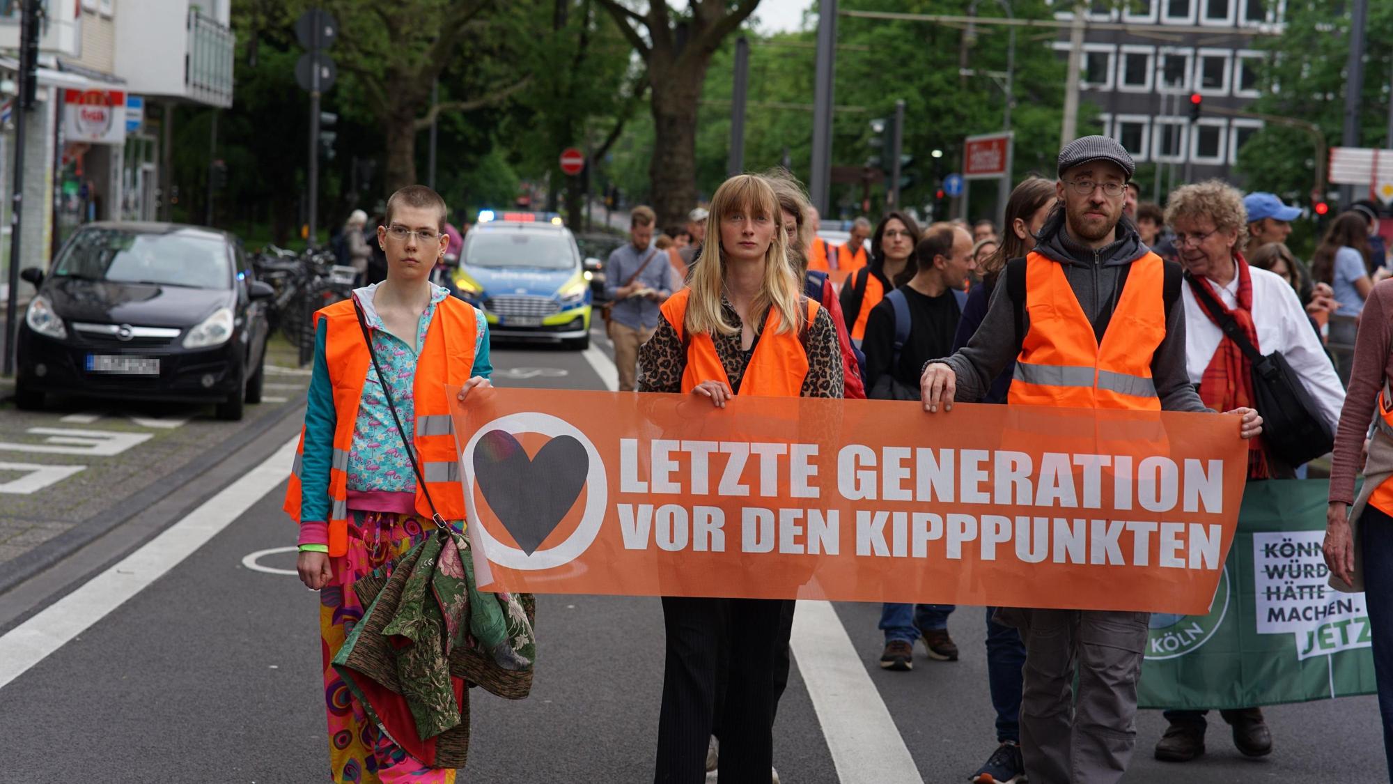 Demonstranten der Letzten Generation laufen eine Straße entlang und halten ein Transparent hoch.