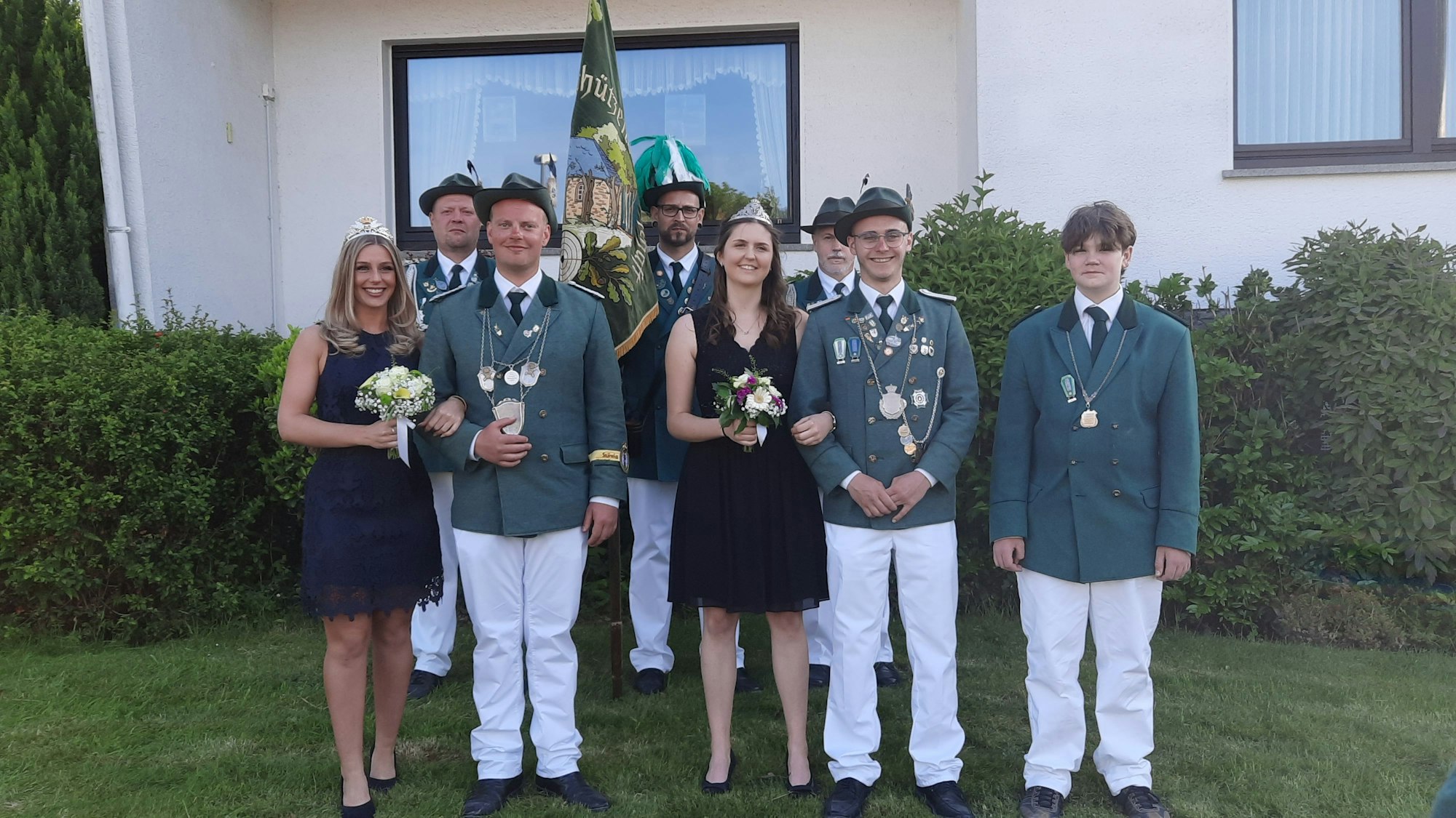 Die Personen stehen in Schützenkleidung vor einem Haus.