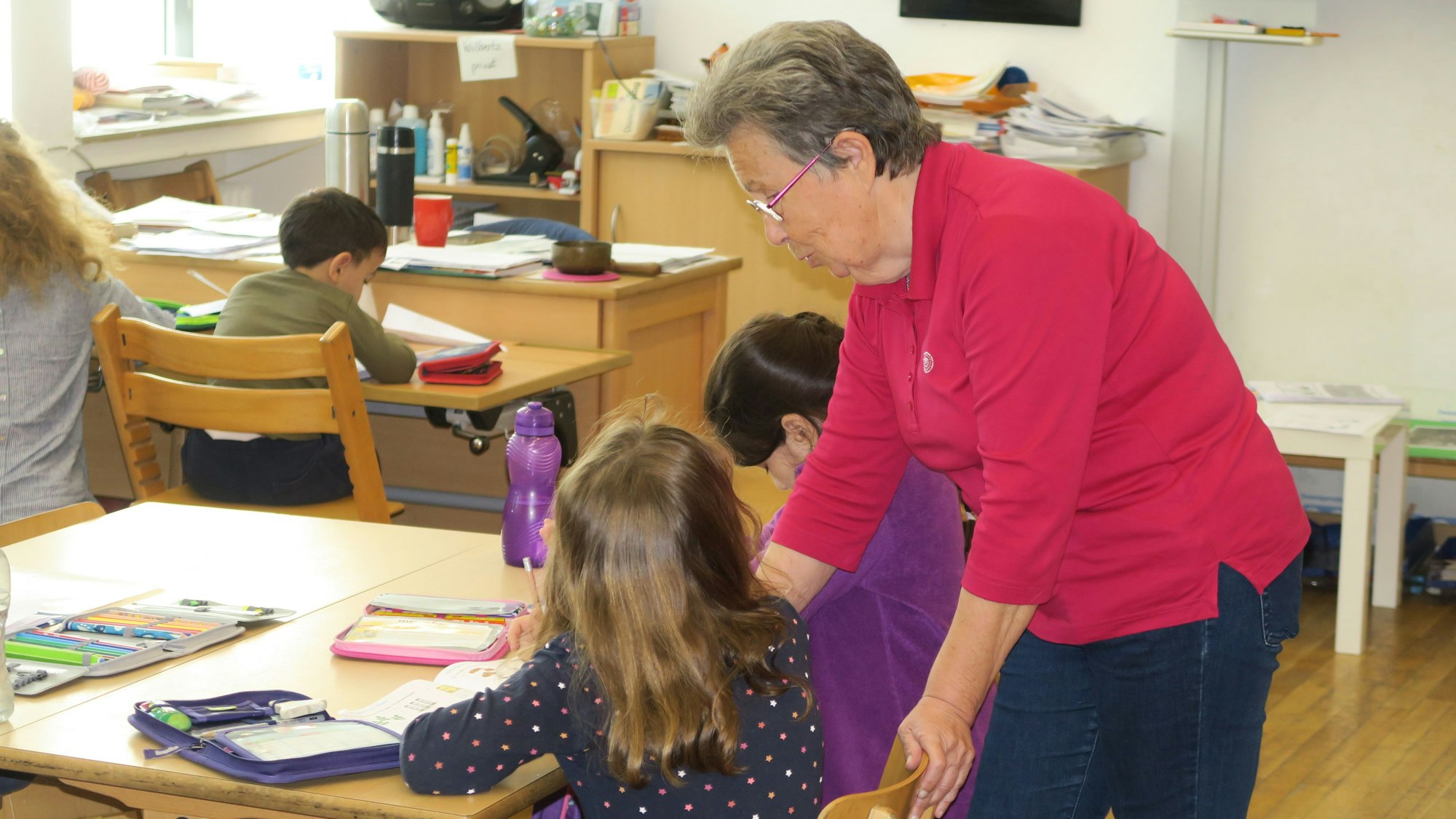 Die Seniorin steht neben einer Schülerin und erklärt ihr eine Aufgabe,