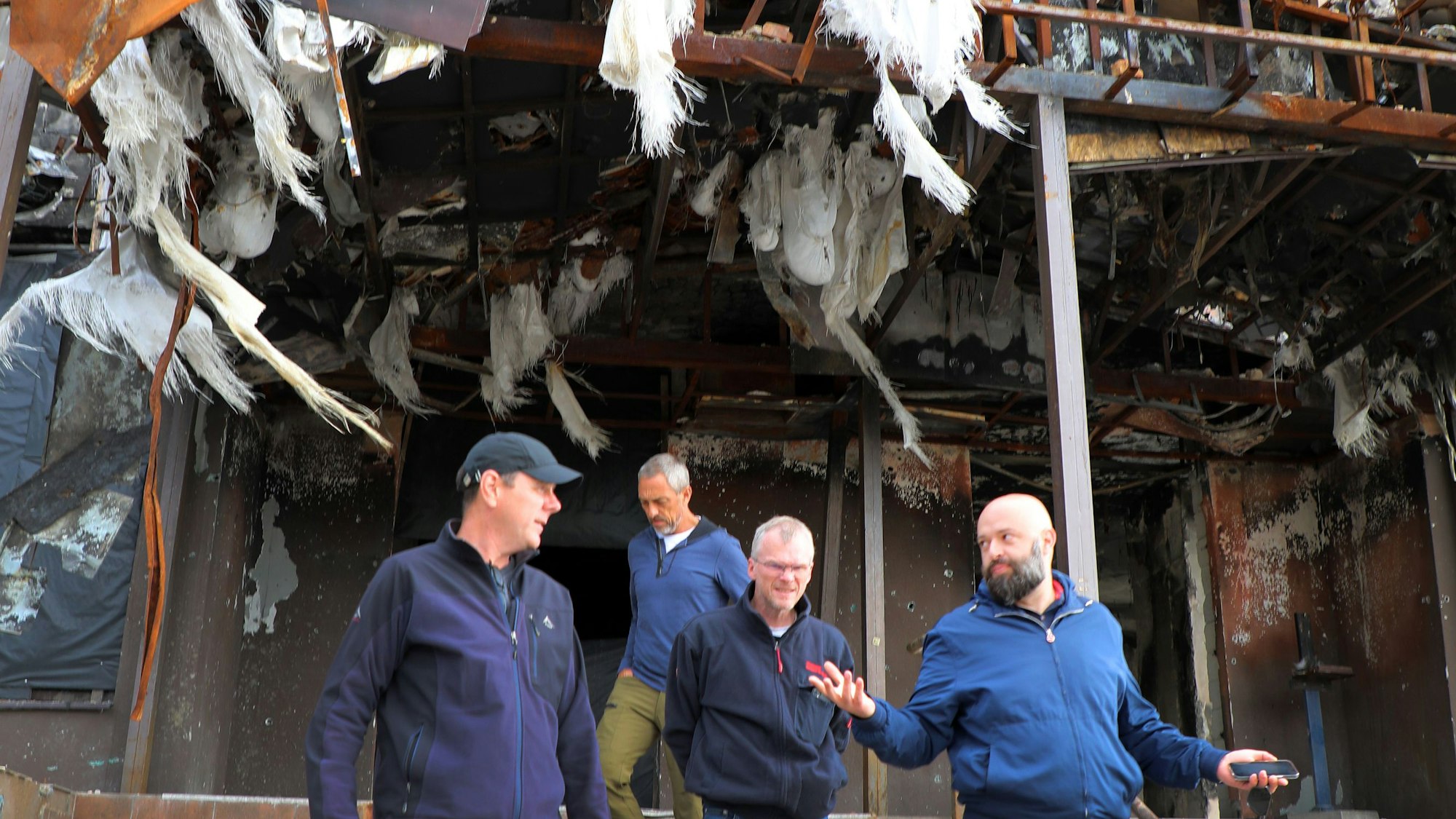 Vier Männer kommen aus einem durch Raketen schwer bschädigten Wohn- und Geschäftshaus.