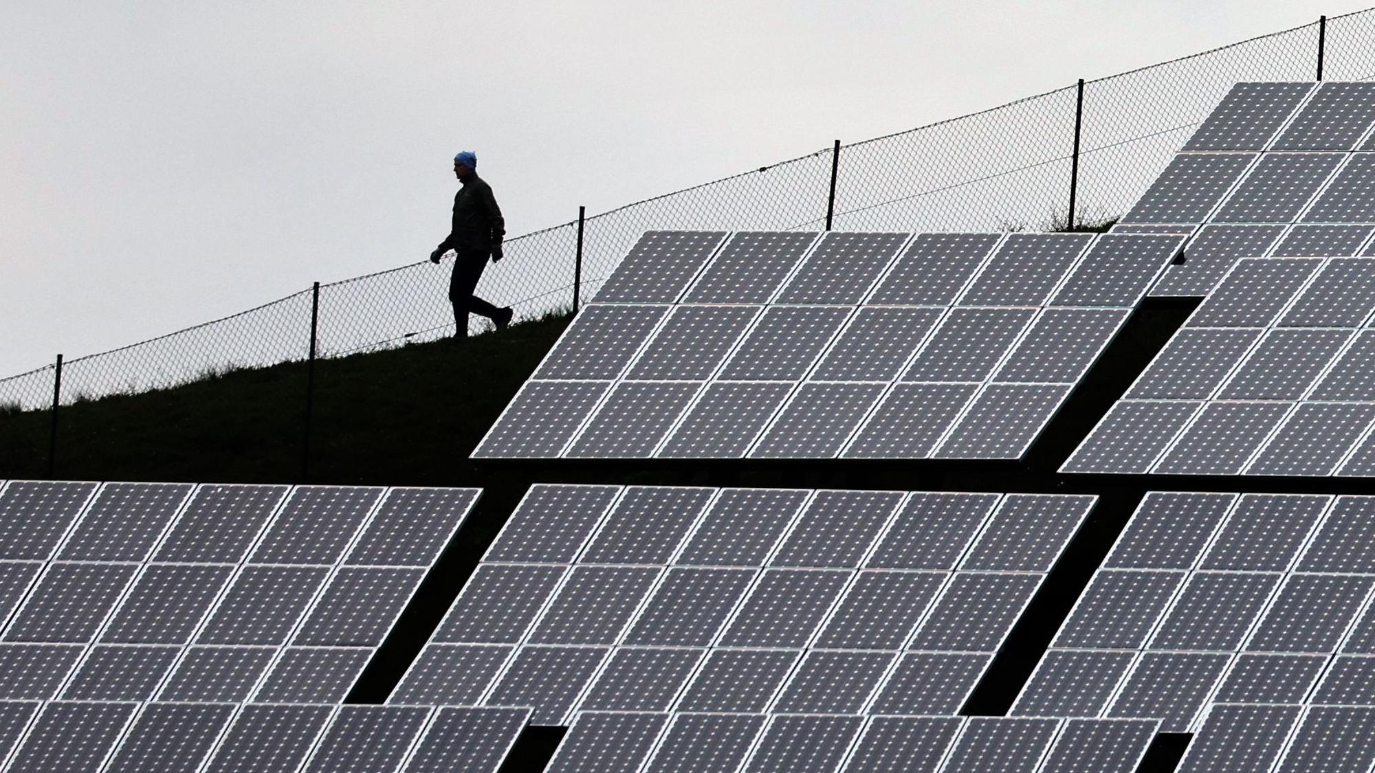 Ein Mensch läuft hinter Solaranlagen her.