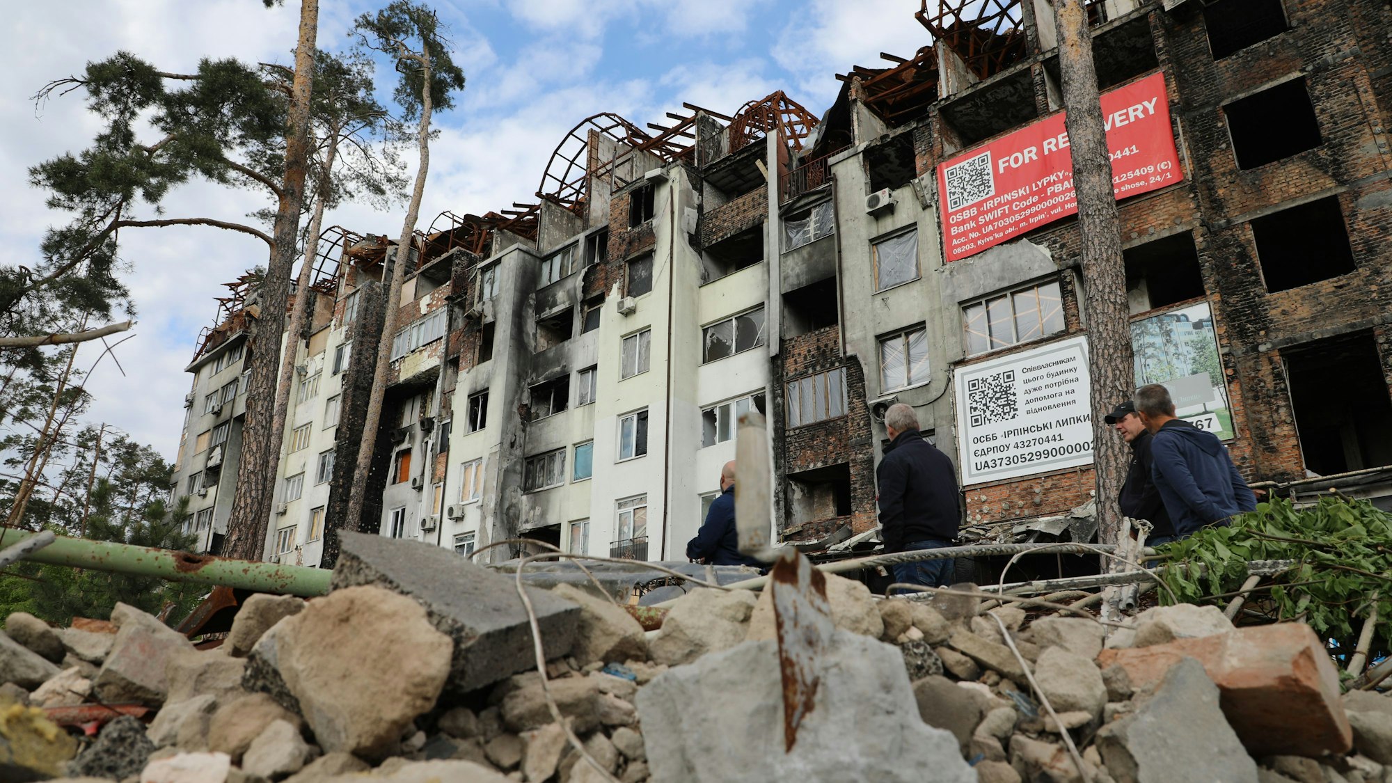 Ein Haus mit ausgebranntem Dach und ausgebrannten Fensterhählen steht hinter einem Berg von Schutt.