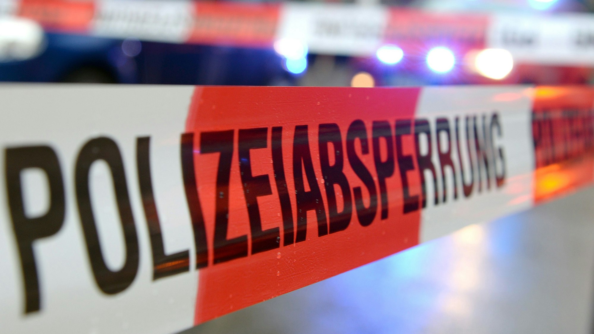 Polizeiabsperrband ist über eine Fläche gespannt. Dahinter steht ein Blaulichtfahrzeug.