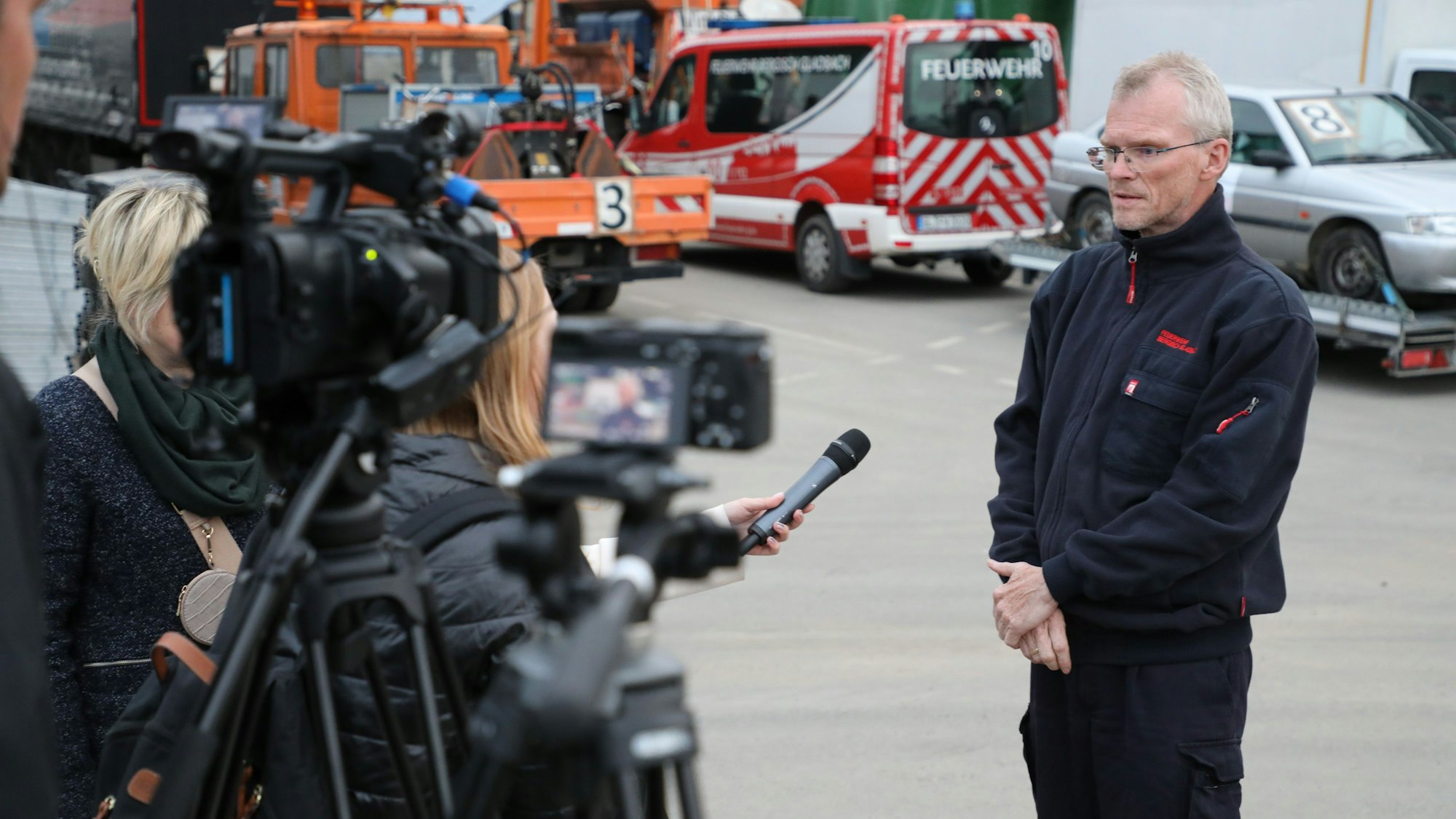 Bergisch Gladbachs Bürgermeister Frank Stein wird vor einer Kamera interviewt. Im Hintergrund sind Fahrzeuge des jüngsten Hilfskonvois nach Butscha zu sehen.