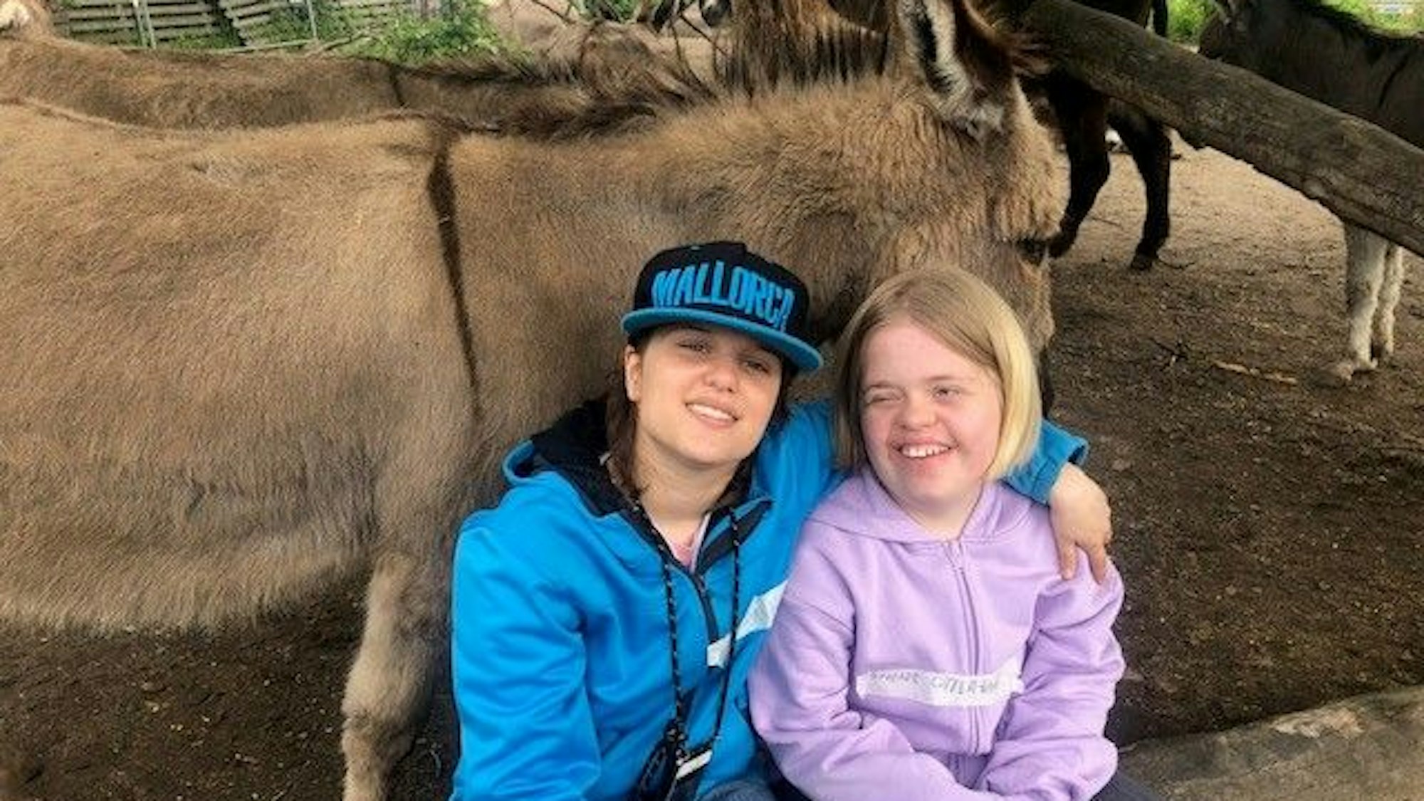 Die 15-jährigen Teenagerinnen Charlotte und Linda halten sich im Arm, hinter ihnen stehen Esel.