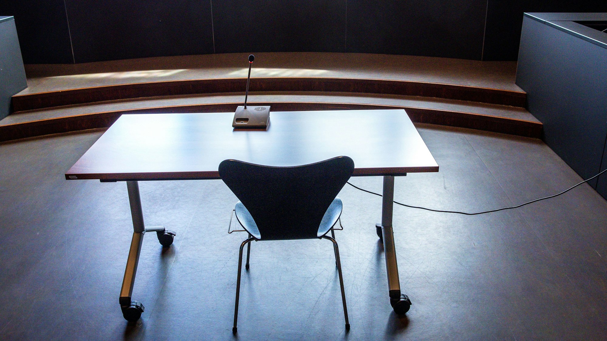Tisch und Stuhl für Zeugenaussagen stehen vor einem Fenster. Auf dem Tisch ein Mikro.