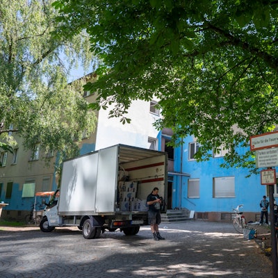 Weißer Lieferwagen vor einem blau angemalten, heruntergekommen aussehenden Gebäude.