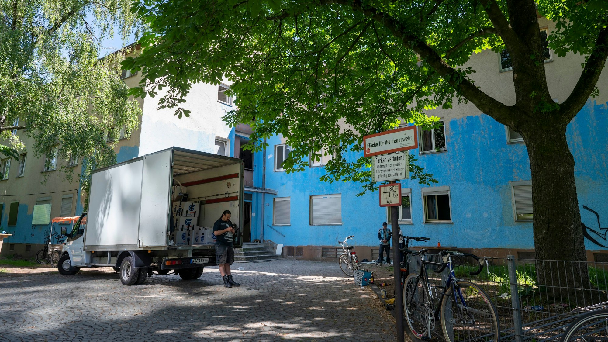 Weißer Lieferwagen vor einem blau angemalten, heruntergekommen aussehenden Gebäude.