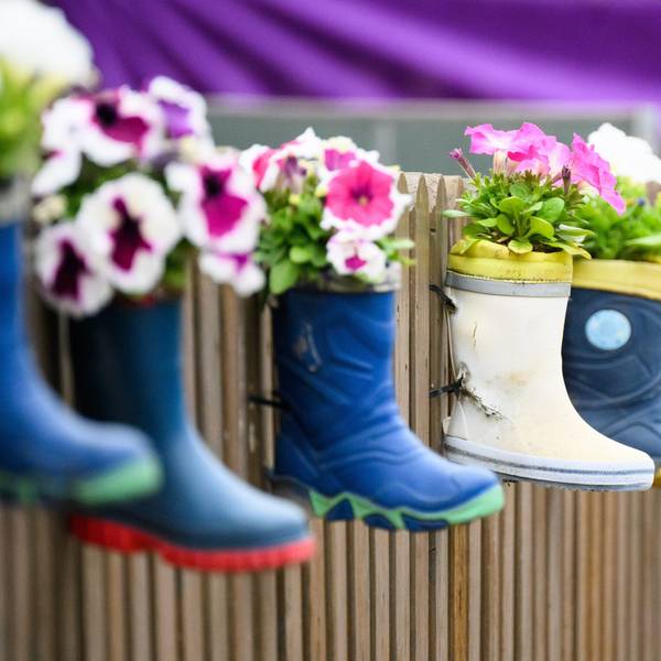 Kinder-Gummistiefel mit Blumen hängen an einem Zaun einer Kindertagesstätte.