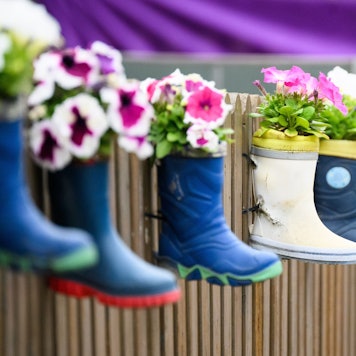 Kinder-Gummistiefel mit Blumen hängen an einem Zaun einer Kindertagesstätte.