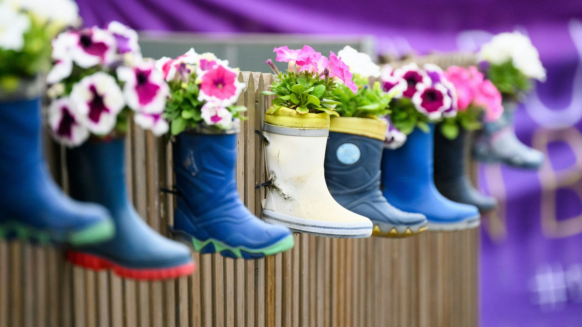Kinder-Gummistiefel mit Blumen hängen an einem Zaun einer Kindertagesstätte.