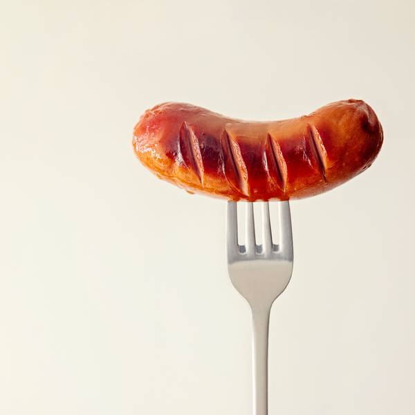 Eine kleine Bratwurst ist auf eine Gabel gespießt.