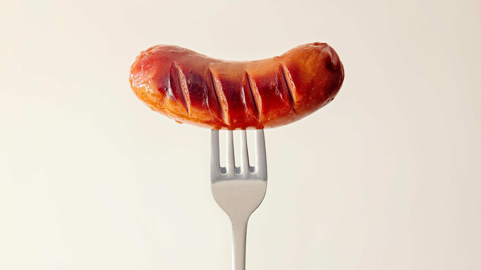 Eine kleine Bratwurst ist auf eine Gabel gespießt.