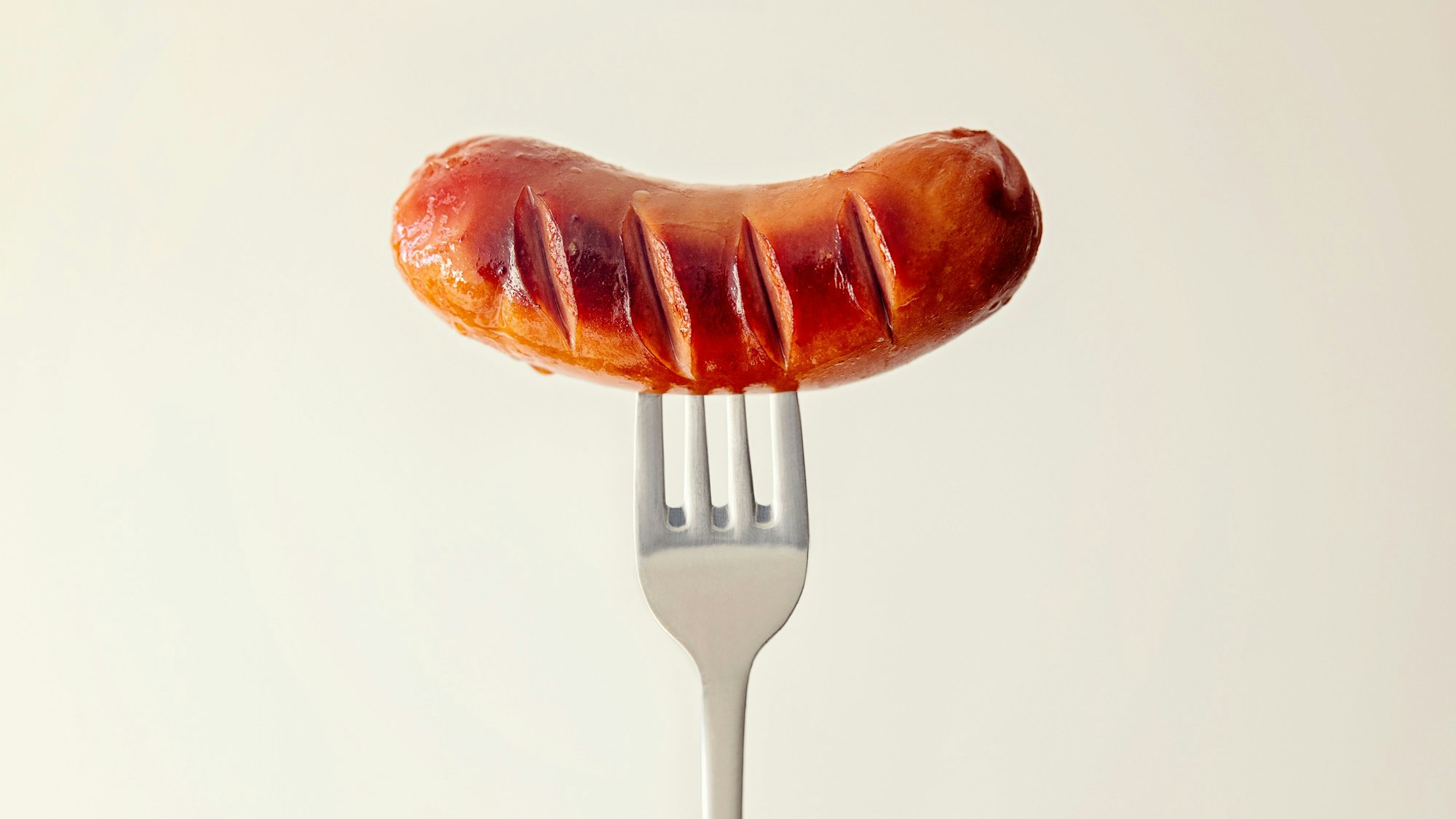 Eine kleine Bratwurst ist auf eine Gabel gespießt.