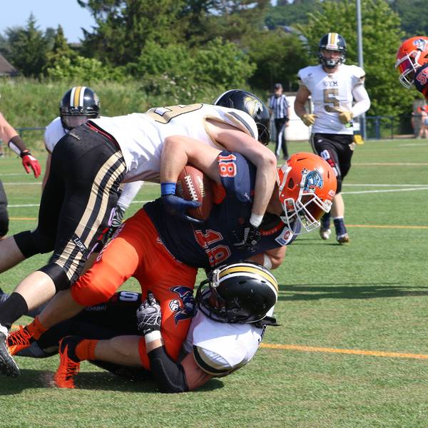 Die Euskirchen Lions (weiss) gewannen gegen die Oberhausen Tornados (blau-orange). Ein Ballträger wird beim American Football von Gegenspielern zu Fall gebracht.