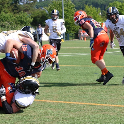 Die Euskirchen Lions (weiss) gewannen gegen die Oberhausen Tornados (blau-orange). Ein Ballträger wird beim American Football von Gegenspielern zu Fall gebracht.