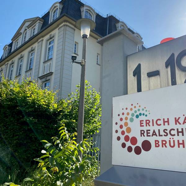 Die Erich-Kästner-Realschule in Brühl ist abgebildet. Die Hausnummer, das Logo der Realschule sowie das Schulgebäude sind zu sehen.