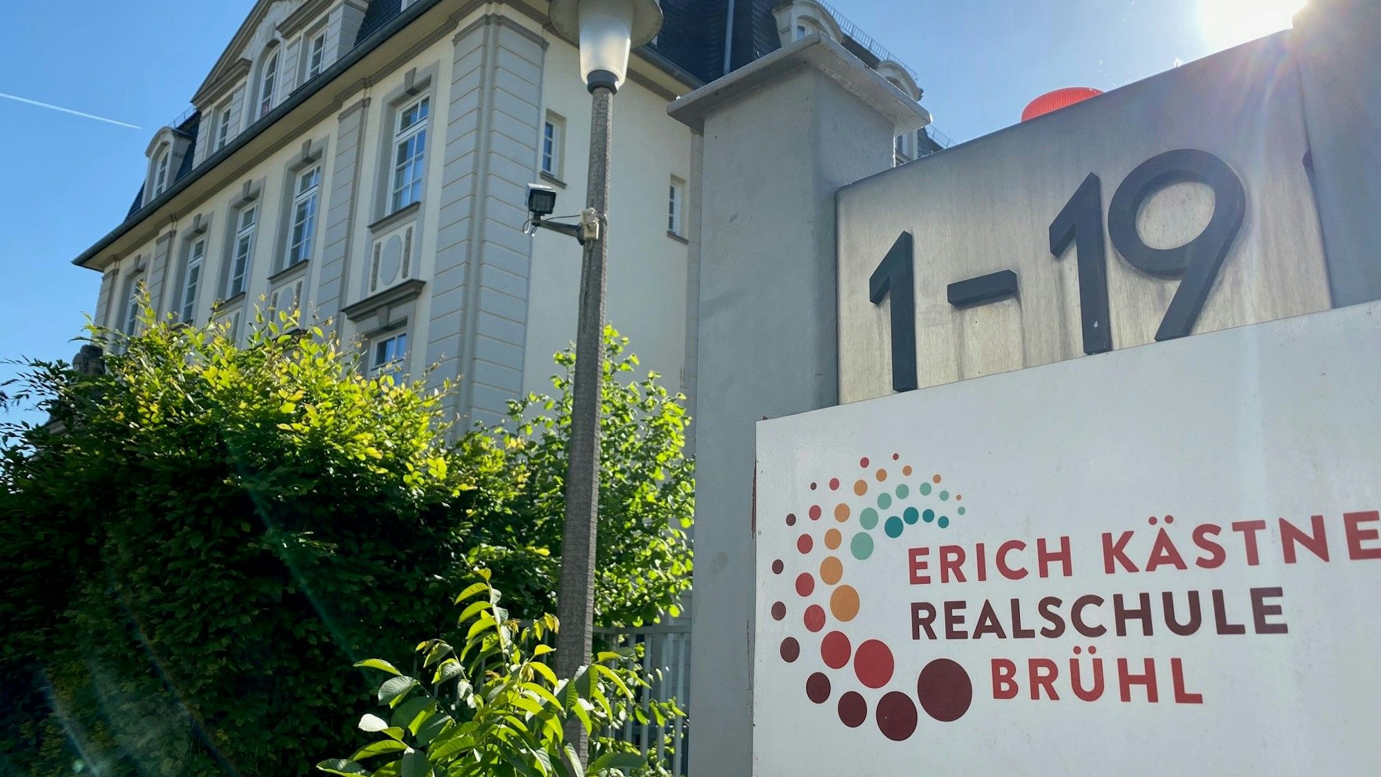 Die Erich-Kästner-Realschule in Brühl ist abgebildet. Die Hausnummer, das Logo der Realschule sowie das Schulgebäude sind zu sehen.