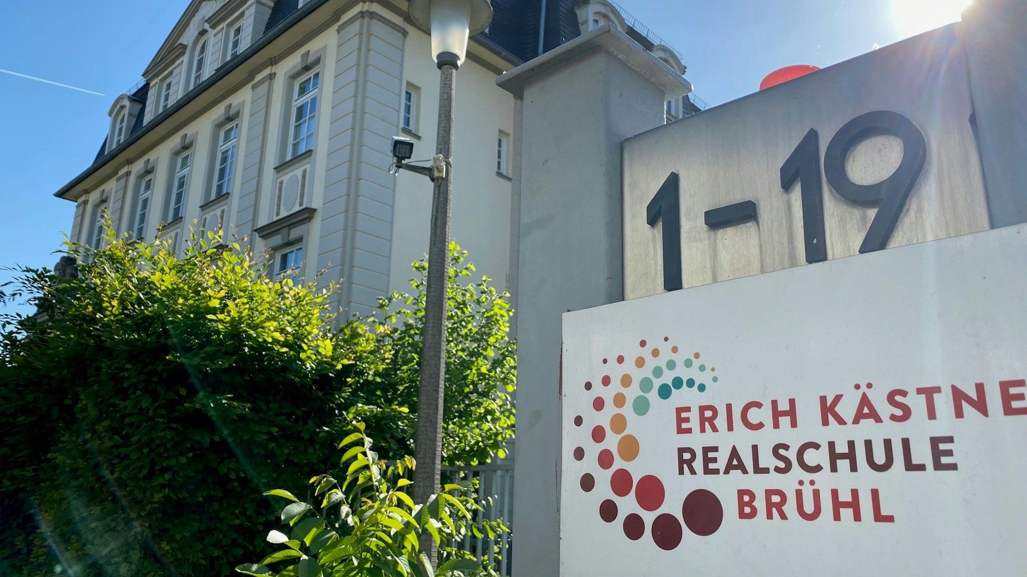 Die Erich-Kästner-Realschule in Brühl ist abgebildet. Die Hausnummer, das Logo der Realschule sowie das Schulgebäude sind zu sehen.