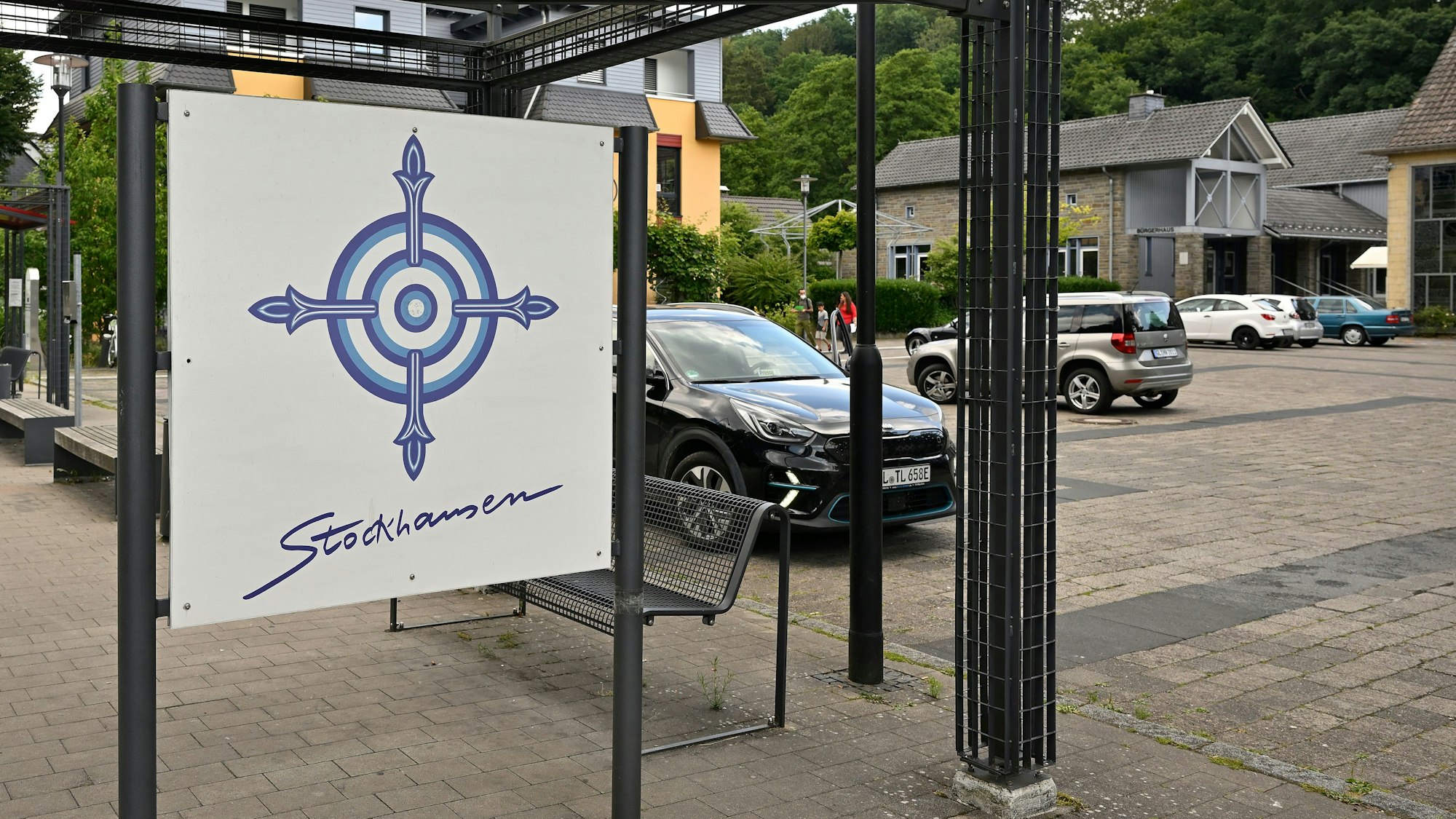 Ein Kunstplakat hängt an einer Metall-Pergola auf einem Parkplatz.